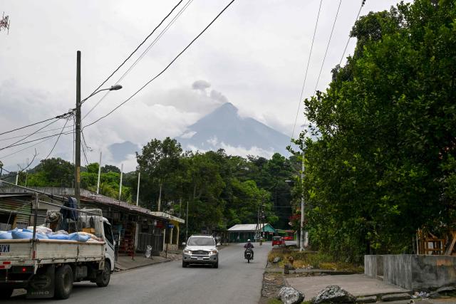 Vehicles drive down a street as the Fuego volcano erupts in Alotenango, some 65 kilometers southwest of Guatemala City, on August 4, 2026. Guatemalan authorities issued the country's second-highest emergency alert level on August 4 after a major eruption of Central America's most active volcano, prompting the evacuation of nearby villages. (Photo by Johan ORDONEZ / AFP)