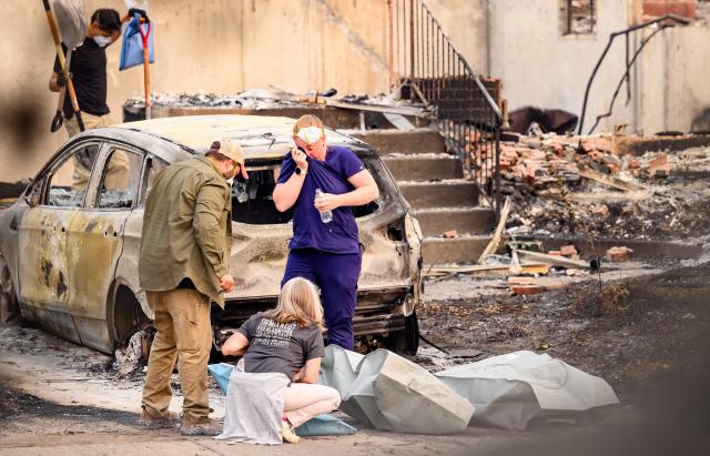 Residents mourn as they place the remains of deceased dogs into body bags at a burned home during the Old Trails fire in Spokane, Washington on August 4, 2026. US authorities arrested a man on August 3, 2026 on suspicion of arson in connection with the biggest of three fires burning around the northwestern city of Spokane, as firefighters raced to contain flames that have displaced tens of thousands. Wildfires supercharged by drought and intense heat have torn through the city in Washington state, burning thousands of acres and reducing hundreds of buildings to cinders while anxious families await news on when they can return. (Photo by Josh Edelson / AFP)