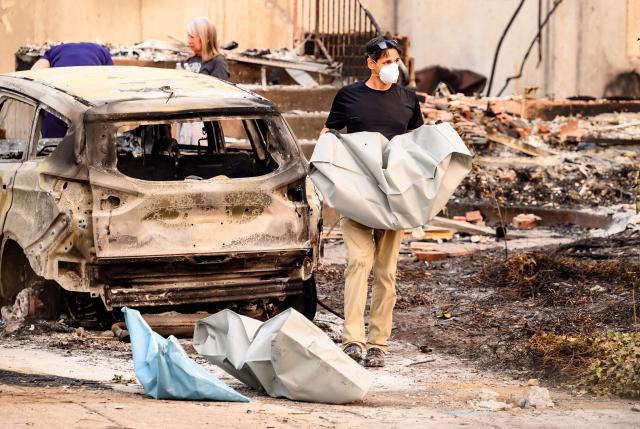 Residents carry the remains of deceased dogs at a burned home during the Old Trails fire in Spokane, Washington on August 4, 2026. US authorities arrested a man on August 3, 2026 on suspicion of arson in connection with the biggest of three fires burning around the northwestern city of Spokane, as firefighters raced to contain flames that have displaced tens of thousands. Wildfires supercharged by drought and intense heat have torn through the city in Washington state, burning thousands of acres and reducing hundreds of buildings to cinders while anxious families await news on when they can return. (Photo by Josh Edelson / AFP)