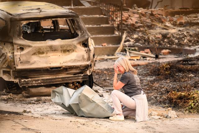 A woman mourns next to a deceased dog at a burned home during the Old Trails fire in Spokane, Washington on August 4, 2026. US authorities arrested a man on August 3, 2026 on suspicion of arson in connection with the biggest of three fires burning around the northwestern city of Spokane, as firefighters raced to contain flames that have displaced tens of thousands. Wildfires supercharged by drought and intense heat have torn through the city in Washington state, burning thousands of acres and reducing hundreds of buildings to cinders while anxious families await news on when they can return. (Photo by Josh Edelson / AFP)