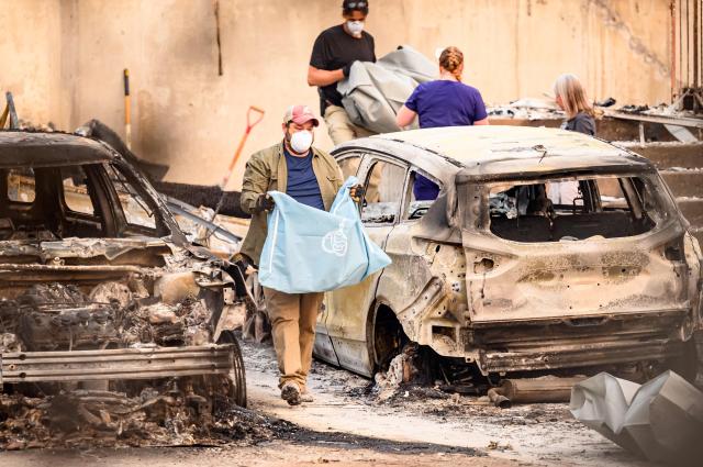 Residents carry the remains of deceased dogs at a burned home during the Old Trails fire in Spokane, Washington on August 4, 2026. US authorities arrested a man on August 3, 2026 on suspicion of arson in connection with the biggest of three fires burning around the northwestern city of Spokane, as firefighters raced to contain flames that have displaced tens of thousands. Wildfires supercharged by drought and intense heat have torn through the city in Washington state, burning thousands of acres and reducing hundreds of buildings to cinders while anxious families await news on when they can return. (Photo by Josh Edelson / AFP)