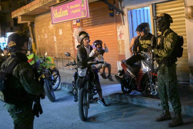 Colombian policemen stand guard as locals ride their motorcycles in the Melendez neighborhood prior to the upcoming presidential inauguration of Colombia's president-elect Abelardo de la Espriella, in Cali, Colombia, on August 4, 2026. De la Espriella's inauguration will take place on August 7, 2026. (Photo by JOAQUIN SARMIENTO / AFP)