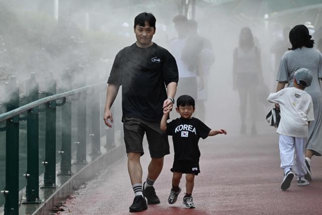 A man and boy walk through mist being sprayed to cool visitors at the Gwangmyeong Cave tourist site in Gyeonggi province on August 5, 2026. South Korea has been sweltering in a streak of searing weather -- new all-time highs were set three times over the past week alone, peaking at 42.5C on August 2. (Photo by GREG BAKER / AFP)