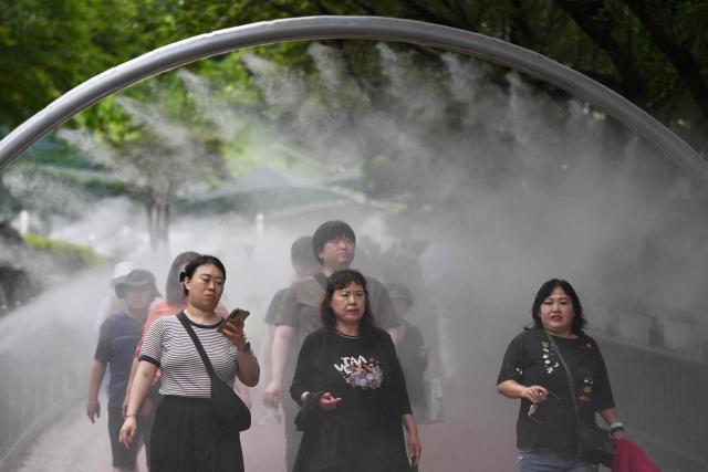 People walk through mist being sprayed to cool visitors at the Gwangmyeong Cave tourist site in Gyeonggi province on August 5, 2026. South Korea has been sweltering in a streak of searing weather -- new all-time highs were set three times over the past week alone, peaking at 42.5C on August 2. (Photo by GREG BAKER / AFP)