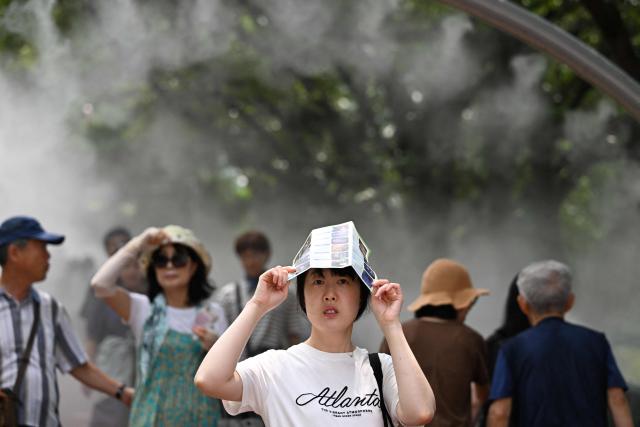 People walk through mist being sprayed to cool visitors at the Gwangmyeong Cave tourist site in Gyeonggi province on August 5, 2026. South Korea has been sweltering in a streak of searing weather -- new all-time highs were set three times over the past week alone, peaking at 42.5C on August 2. (Photo by GREG BAKER / AFP)