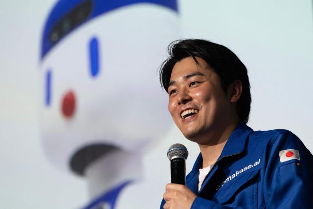 Zeals CEO Masahiro Shimizu speaks near a picture of the company's semi-domestic compact humanoid "D1" helper robot during a press preview at Shibuya Scramble Hall in Tokyo on August 5, 2026. (Photo by Andrew CABALLERO-REYNOLDS / AFP)