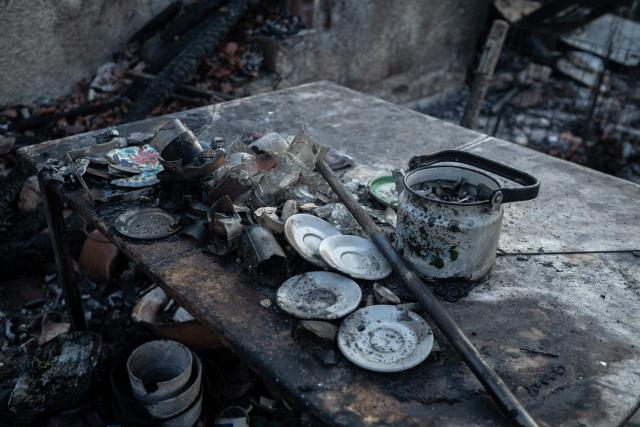 This photograph taken on August 5, 2026, shows burnt household items on a table inside a house destroyed by a wildfire in Porto Germeno, some 70 kilometres (45 miles) northwest of Athens. Greek officials and residents of a region west of the capital Athens on August 5, 2026, began to assess the damage suffered by homes, businesses and farmland scorched by a wildfire. (Photo by Angelos TZORTZINIS / AFP)