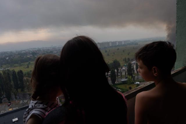 TOPSHOT - A Ukrainian family stand on a balcony to watch smoke rising from a fire following massive Russian ballistic missile and drone strikes in Kyiv on August 5, 2026, amid the Russian invasion of Ukraine. Russian strikes on Ukraine's capital and surrounding region killed at least two people and wounded dozens more, authorities said on August 5, 2026, after fresh overnight missile and drone attacks. (Photo by Tetiana DZHAFAROVA / AFP)