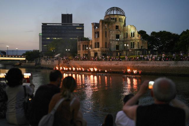People stand along the Motoyasu river as Kagaribi, ceremonial bonfires, are lit in front of the Atomic Bomb Dome to remember the victims on the eve of the 81st anniversary of the world's first atomic bomb attack, in Hiroshima on August 5, 2026. (Photo by JIJI Press / AFP) / Japan OUT