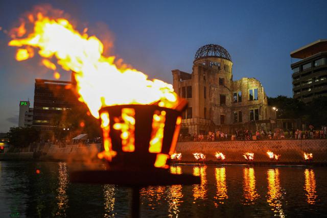 People stand along the Motoyasu river as Kagaribi, ceremonial bonfires, are lit in front of the Atomic Bomb Dome to remember the victims on the eve of the 81st anniversary of the world's first atomic bomb attack, in Hiroshima on August 5, 2026. (Photo by JIJI Press / AFP) / Japan OUT