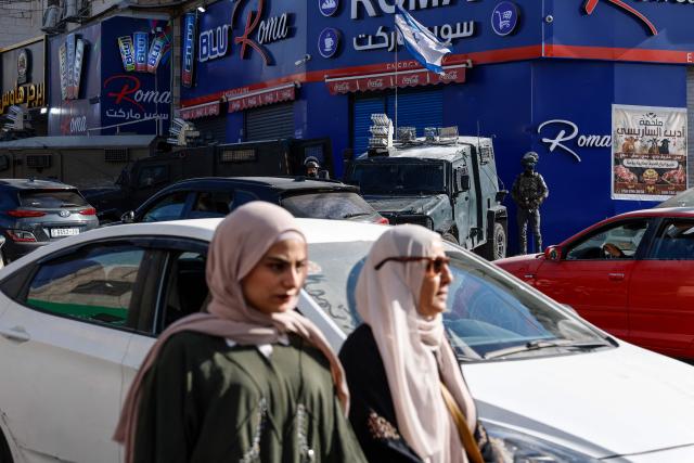 Women walk past Israeli security forces deployed on a street during a military raid in the Qalandia refugee camp, south of Ramallah in the Israeli-occupied West Bank, on August 5, 2026. Since the start of the Gaza war in October 2023, violence has escalated in the West Bank, which Israel has occupied since 1967. (Photo by Zain JAAFAR / AFP)