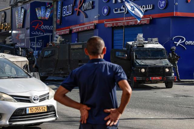 A man stands in front of Israeli security forces deployed on a street during a military raid in the Qalandia refugee camp, south of Ramallah in the Israeli-occupied West Bank, on August 5, 2026. Since the start of the Gaza war in October 2023, violence has escalated in the West Bank, which Israel has occupied since 1967. (Photo by Zain JAAFAR / AFP)