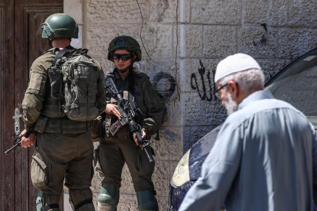 A man walks past Israeli security forces patrolling along a street during a military raid in the Qalandia refugee camp, south of Ramallah in the Israeli-occupied West Bank, on August 5, 2026. Since the start of the Gaza war in October 2023, violence has escalated in the West Bank, which Israel has occupied since 1967. (Photo by Zain JAAFAR / AFP)