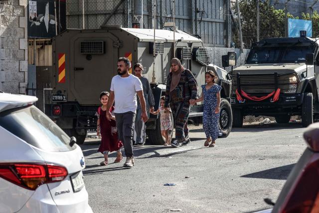 Palestinians walk past Israeli security forces deployed on a street during a military raid in the Qalandia refugee camp, south of Ramallah in the Israeli-occupied West Bank, on August 5, 2026. Since the start of the Gaza war in October 2023, violence has escalated in the West Bank, which Israel has occupied since 1967. (Photo by Zain JAAFAR / AFP)