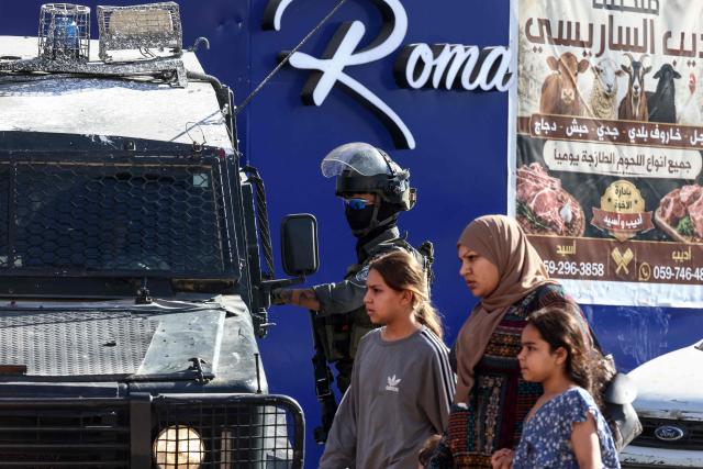 Palestinians walk past Israeli security forces deployed on a street during a military raid in the Qalandia refugee camp, south of Ramallah in the Israeli-occupied West Bank, on August 5, 2026. Since the start of the Gaza war in October 2023, violence has escalated in the West Bank, which Israel has occupied since 1967. (Photo by Zain JAAFAR / AFP)
