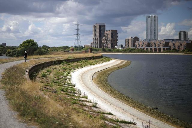 A pedestrian (L) walks along the path around Lockwood Reservoir near Walthamstow in north London on August 5, 2026, as the UK Met Office weather agency said on August 3 that England and Wales both experienced the "driest July on record". London and its suburbs are one of 19 English regions to have had no more than one millimetre of rainfall in July, with water companies in parts of England and Wales imposing bans on using hose pipes for household tasks and watering plants. (Photo by Henry Nicholls / AFP)