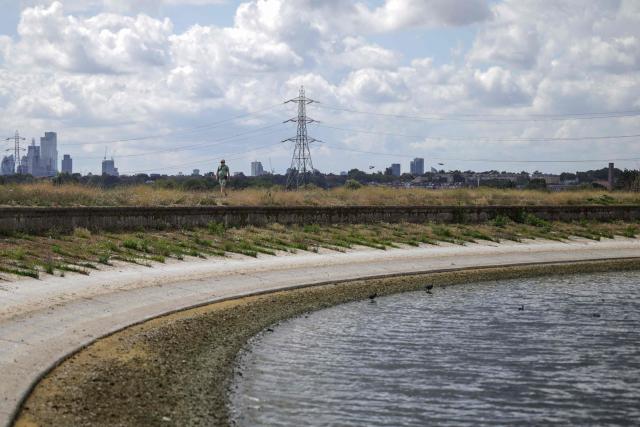 A pedestrian (top L) walks along the path around Lockwood Reservoir near Walthamstow in north London on August 5, 2026, as the UK Met Office weather agency said on August 3 that England and Wales both experienced the "driest July on record". London and its suburbs are one of 19 English regions to have had no more than one millimetre of rainfall in July, with water companies in parts of England and Wales imposing bans on using hose pipes for household tasks and watering plants. (Photo by Henry Nicholls / AFP)