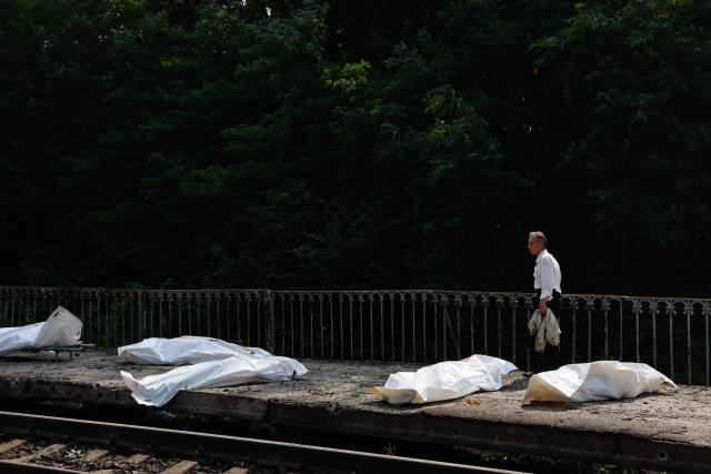 EDITORS NOTE: Graphic content / A man walks past bodies in plastic bags of people killed during aRussian ballistic missile and drone strikes at a railway station in the Kyiv region on August 5, 2026, amid the Russian invasion of Ukraine. Russian missile and drone strikes killed at least 17 people and wounded dozens more in Kyiv and the surrounding region overnight, authorities said on August 5, 2026. (Photo by Mykola Tymchenko / AFP)