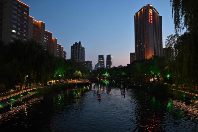 People paddle along the Liangma river at dusk in Beijing on August 5, 2026. (Photo by ADEK BERRY / AFP)