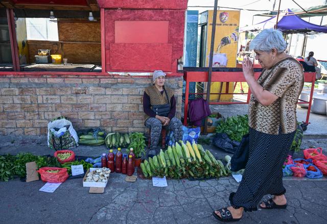 A woman walks-by and greets a seller with home made products and produce spread on the ground at the open-air market in the city of Calarasi, Romania, on July 26, 2026. As the eastern European country has struggled for months with the highest inflation in the European Union, almost 11 percent in May, several buyers complained of rising prices which forced them to make difficult decisions about what to cut. (Photo by Daniel MIHAILESCU / AFP)