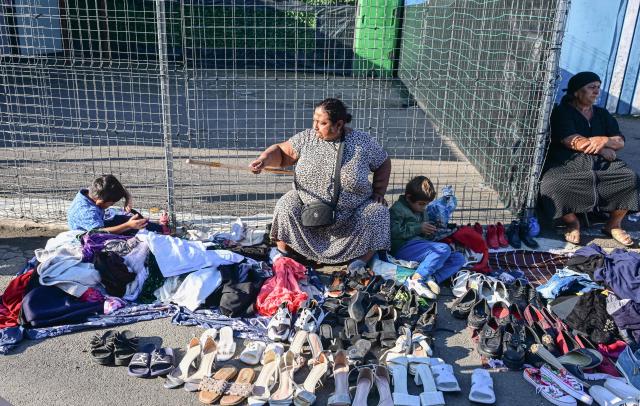 A woman gestures as she sells second hand shoes spread on the ground with two children chilling near her at the open-air market in the city of Calarasi, Romania, on July 26, 2026. As the eastern European country has struggled for months with the highest inflation in the European Union, almost 11 percent in May, several buyers complained of rising prices which forced them to make difficult decisions about what to cut. (Photo by Daniel MIHAILESCU / AFP)