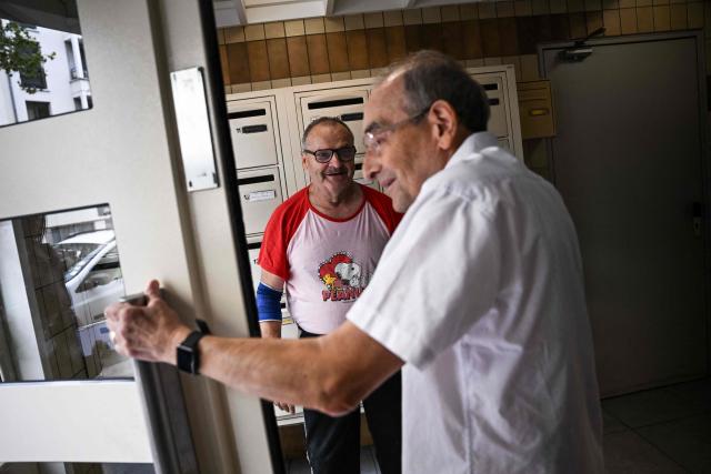 Maurice, 67, speaks with Stanislas (R) working with charity organisation Les Petits Freres des Pauvres, in the entrance hall of his apartment building in Colombes, suburb of Paris on August 5, 2026. On June 27, 2026 Matignon, France's Prime Minister's Office called for "everyone to remain vigilant", confirming, as previously noted by Health Minister, "an increase in the number of deaths, mainly occurring at home, consistent with a delayed peak" and linked to "the isolation of some elderly or vulnerable people." Two million additional elderly people will be automatically added to municipal registers that identify vulnerable individuals during heatwaves, under a decree published two years after the law providing for the measure was passed, the Health Ministry said in early July 2026. (Photo by Lou BENOIST / AFP)