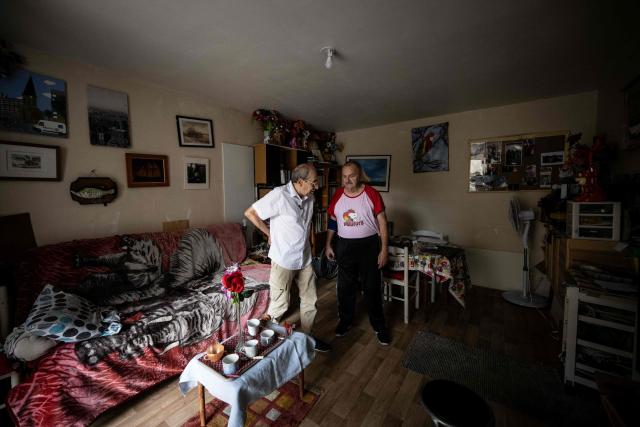 Maurice, 67, speaks with Stanislas (L) working with charity organisation Les Petits Freres des Pauvres, at his apartment in Colombes, suburb of Paris on August 5, 2026. On June 27, 2026 Matignon, France's Prime Minister's Office called for "everyone to remain vigilant", confirming, as previously noted by Health Minister, "an increase in the number of deaths, mainly occurring at home, consistent with a delayed peak" and linked to "the isolation of some elderly or vulnerable people." Two million additional elderly people will be automatically added to municipal registers that identify vulnerable individuals during heatwaves, under a decree published two years after the law providing for the measure was passed, the Health Ministry said in early July 2026. (Photo by Lou BENOIST / AFP)