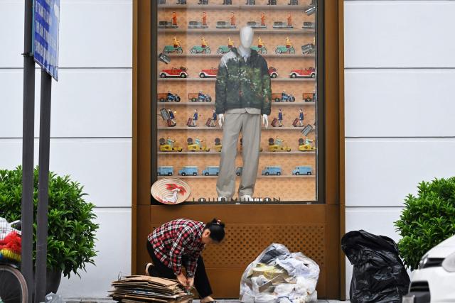 A woman collecting scrap materials bundles cardboard in front of a fashion store in Hanoi on August 6, 2026. (Photo by Nhac NGUYEN / AFP)