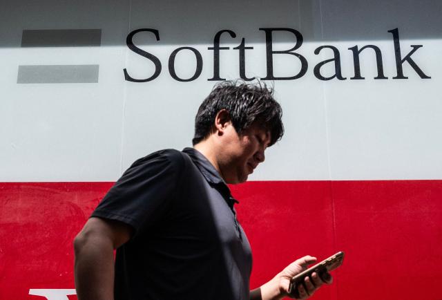 A commuter checks his phone as he walks past a Softbank logo on the side of a building in Tokyo on August 6, 2026. (Photo by Andrew CABALLERO-REYNOLDS / AFP)