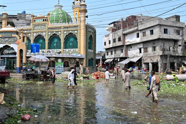 People wade through a waterlogged road at a vegetable market following heavy rainfall in Lahore on August 6, 2026. (Photo by Arif ALI / AFP)