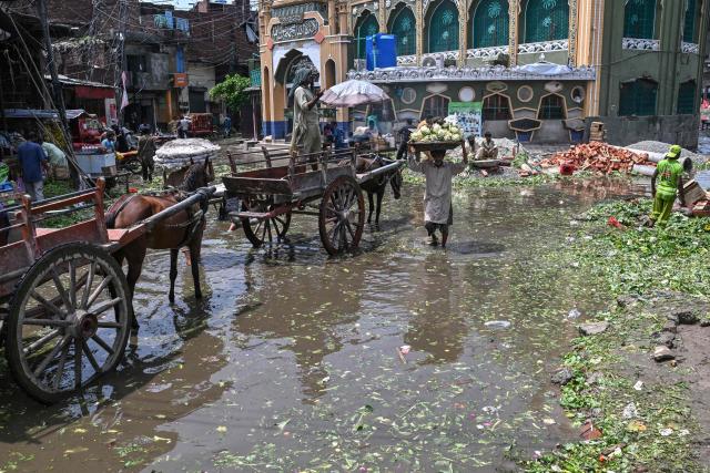 People wade through a waterlogged road at a vegetable market following heavy rainfall in Lahore on August 6, 2026. (Photo by Arif ALI / AFP)