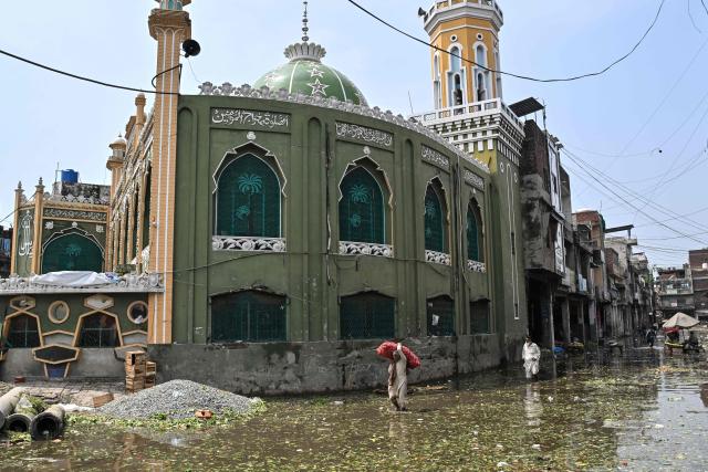 A worker carrying a sack of potatoes wades through a flooded vegetable market following heavy rainfall in Lahore on August 6, 2026. (Photo by Arif ALI / AFP)