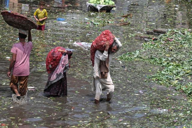 People carrying sacks of vegetables wade through a flooded market following heavy rainfall in Lahore on August 6, 2026. (Photo by Arif ALI / AFP)