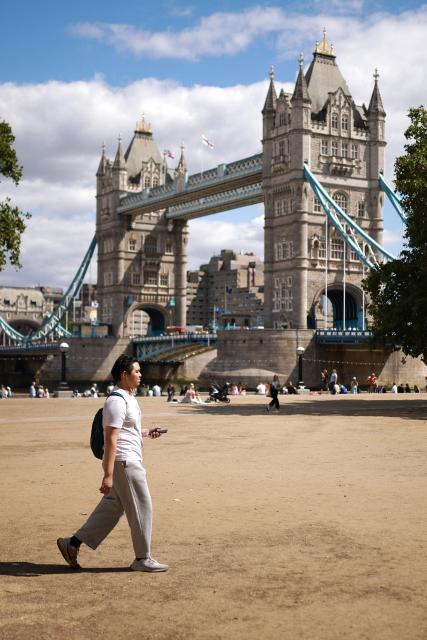 People walk across dry parched grass, turned yellow-brown due to a lack of rain, near Tower Bridge in London on August 6, 2026. London and its suburbs are one of 19 English regions to have had no more than one millimetre of rainfall in July, with water companies in parts of England and Wales imposing bans on using hose pipes for household tasks and watering plants. (Photo by Henry NICHOLLS / AFP)