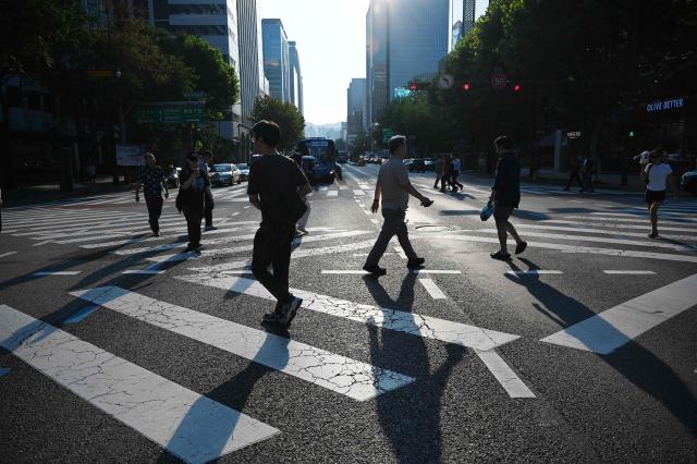 People cross an intersection on a hot day in Seoul on August 6, 2026. South Korea has been sweltering in a streak of searing weather -- new all-time highs were set three times over the past week alone, peaking at 42.5C on August 2. (Photo by GREG BAKER / AFP)