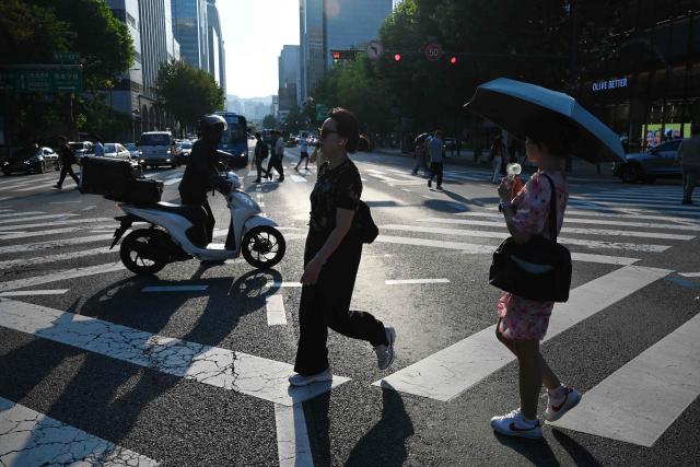 People cross an intersection on a hot day in Seoul on August 6, 2026. South Korea has been sweltering in a streak of searing weather -- new all-time highs were set three times over the past week alone, peaking at 42.5C on August 2. (Photo by GREG BAKER / AFP)