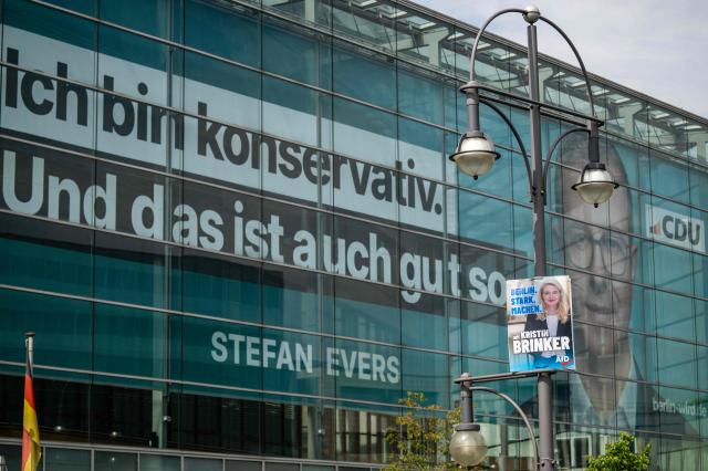 An election placard featuring a portrait of the Alternative for Germany - AfD's main candidate Kristin Brinker, hangs on a strrt light in front of the facade of the CDU headquarters featuring a giant banner with a portrait of Stefan Evers, the Christian Democratic Union's (CDU) main candidate in upcoming regional elections in Berlin, hangs over in Berlin on August 5, 2026. Berlin goes to the polls on September 20, 2026. Slogan on banner reads: "I'm conservative and that's fine by me", a reference to former Berlin mayor Klaus Wowereit's famous coming out quote: "Ich bin Schwul und das ist auch gut so". (I'm gay and that's fine by me) (Photo by John MACDOUGALL / AFP)