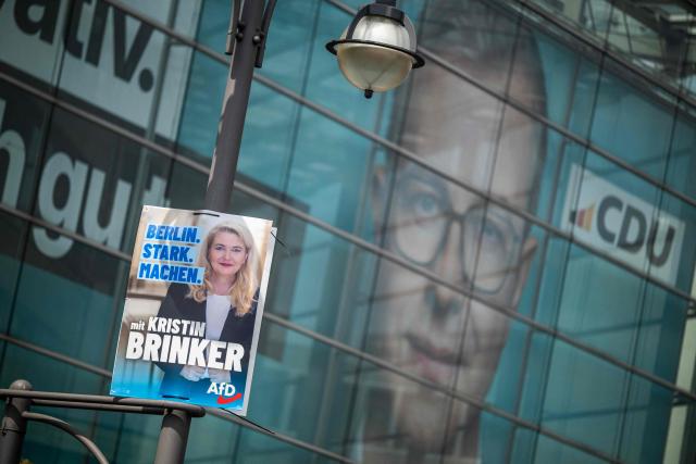 An election placard featuring a portrait of the Alternative for Germany - AfD's main candidate Kristin Brinker, hangs on a strrt light in front of the facade of the CDU headquarters featuring a giant banner with a portrait of Stefan Evers, the Christian Democratic Union's (CDU) main candidate in upcoming regional elections in Berlin, hangs over in Berlin on August 5, 2026. Berlin goes to the polls on September 20, 2026. Slogan on banner reads: "I'm conservative and that's fine by me", a reference to former Berlin mayor Klaus Wowereit's famous coming out quote: "Ich bin Schwul und das ist auch gut so". (I'm gay and that's fine by me) (Photo by John MACDOUGALL / AFP)