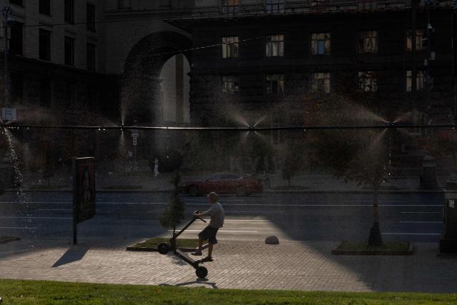 A boy rides an electric scooter near water misters during a hot summer’s day in Kyiv on August 6, 2026, amid the Russian invasion of Ukraine. (Photo by Tetiana DZHAFAROVA / AFP)