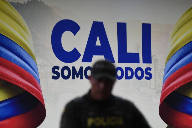 A police officer stands guard in front of a billboard bearing the slogan "Cali Somos Todos" (We Are All Cali) in Cali, Colombia, on August 6, 2026, on the eve of the inauguration of Colombian president-elect Abelardo de la Espriella. (Photo by Jaime SALDARRIAGA / AFP)
