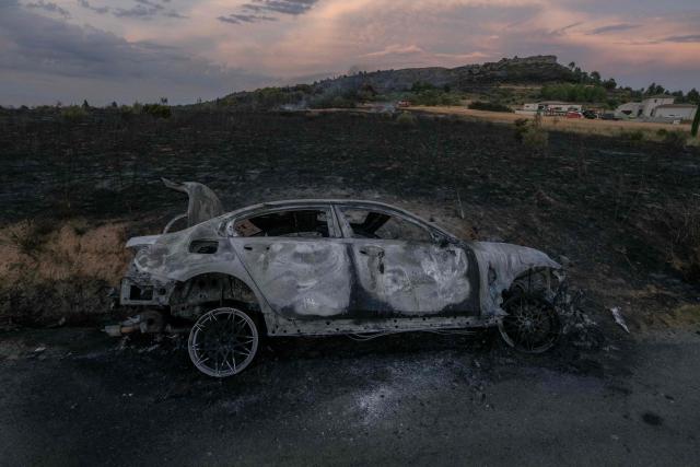 This photograph shows the wreck of a car on the side of the road during a wildfire in the Corbieres massif near Montseret, south-western France on August 6, 2026. A fire caused on August 6, 2026, by a road accident has already spread across around 100 hectares in the Corbières mountains, near Narbonne, not far from the area where 11,000 hectares were burnt a year ago, according to the prefecture. (Photo by Idriss Bigou-Gilles / AFP)