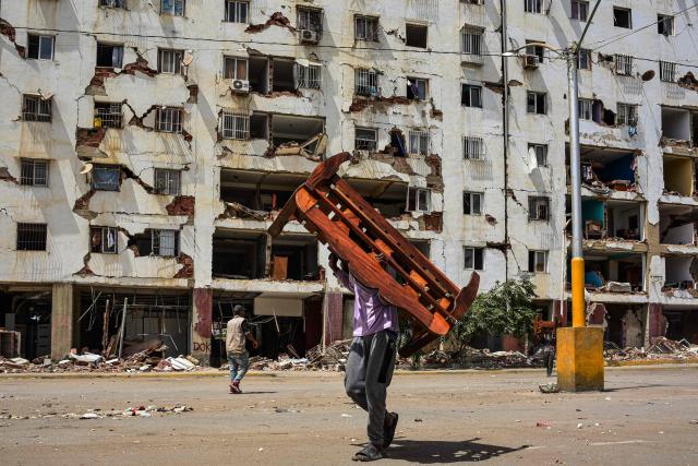 A man carries a piece of furniture salvaged from his apartment in one of the buildings affected by the June 24 earthquake in La Guaira, Venezuela, on August 6, 2026. (Photo by Maxwell BRICENO / AFP)