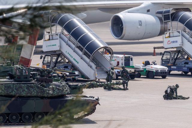 A Taiwanese military M1A2T tank is pictured next to an aircraft during a drill simulating an enemy airborne assault at Taiwan Taoyuan International Airport in Taoyuan on August 7, 2026. Taiwan's largest military drills of the year began on August 5 as the island democracy attempts to prepare its population for a potential Chinese invasion. (Photo by CHENG Yu-chen / AFP)
