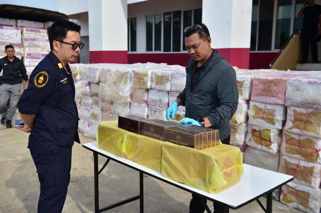 Thai customs officials stand next to confiscated cigarette cartons following an operation to seize the smuggled items worth over 20 million THB (600,000 USD) at the Narathiwat Provincial Police Station in the southern Thai province of Narathiwat on August 7, 2026. (Photo by Madaree TOHLALA / AFP)