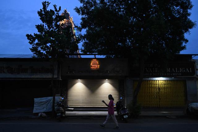 A woman walks past closed shops, at dawn in Chennai on August 7, 2026. (Photo by R.Satish BABU / AFP)
