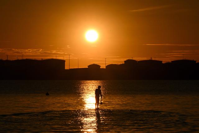 This picture taken on August 6, 2026, shows a paddle boarder silhouetted against the setting sun on a winter evening in Sydney. (Photo by Saeed KHAN / AFP)