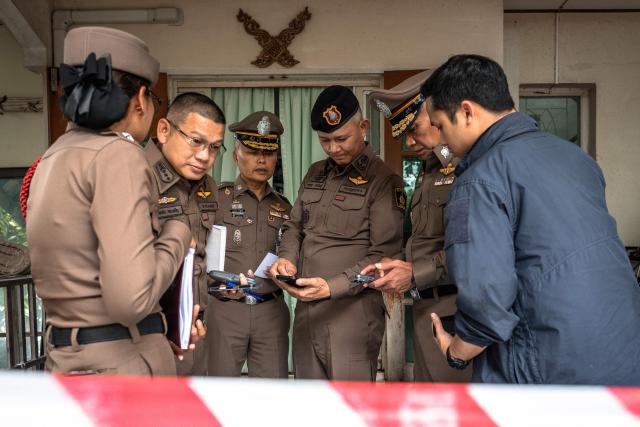 Police look at phones outside the house where a teenage suspect is suspected of killing his grandparents before carrying out a school shooting in Nonthaburi province, north of Thailand's capital Bangkok, on August 7, 2026. A teenage suspect killed his grandparents before shooting dead at least six more people at a school near Bangkok on August 7, police said. (Photo by Chanakarn LAOSARAKHAM / AFP)