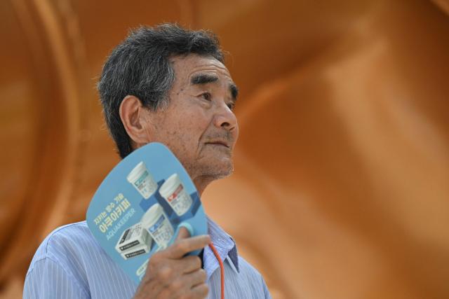 A man fans himself on a hot day in Seoul on August 7, 2026. South Korea has been sweltering in a streak of searing weather -- new all-time highs were set three times over the past week alone, peaking at 42.5C on August 2. (Photo by Greg Baker / AFP)