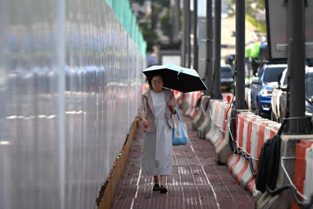 A woman walks on a temporary sidewalk on a hot day in Seoul on August 7, 2026. South Korea has been sweltering in a streak of searing weather -- new all-time highs were set three times over the past week alone, peaking at 42.5C on August 2. (Photo by Greg Baker / AFP)