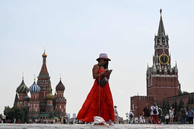 A woman uses her smartphone in Red Square, with the Kremlin's Spasskaya tower and St. Basil's cathedral in the background, on a hot day in central Moscow on August 7, 2026. (Photo by Igor IVANKO / AFP)